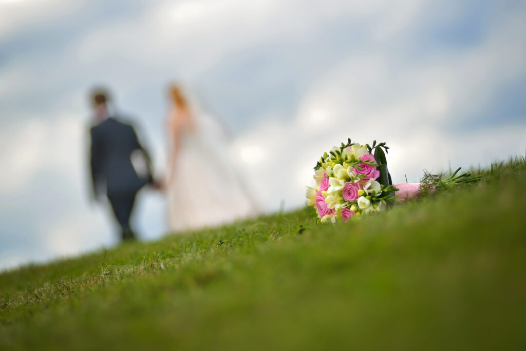 wedding bouquet lying on the grass with a married couple in the background