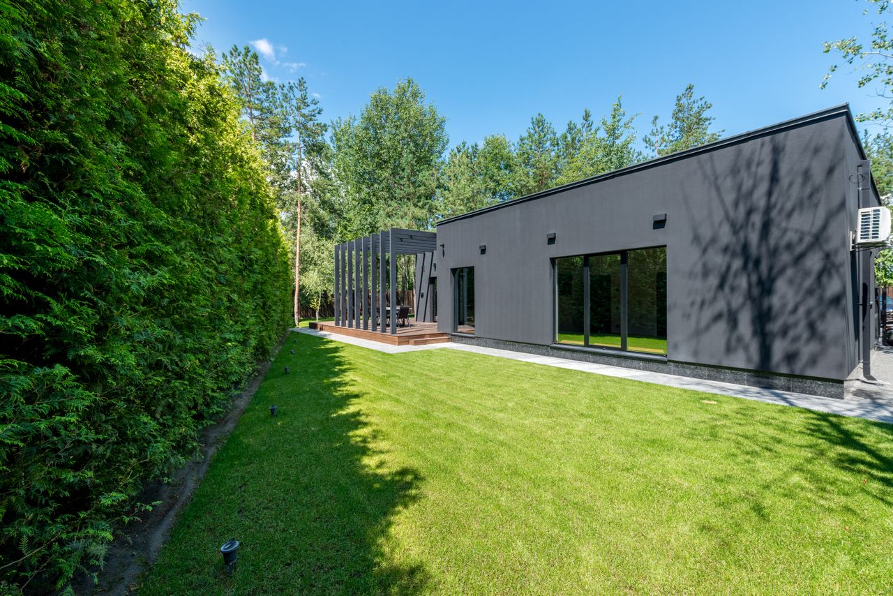 services-03 Sleek black modern house with large windows and vibrant green lawn surrounded by dense trees.